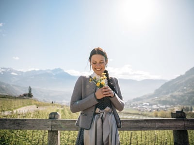 Frau in Tracht hält Blumenstrauß vor Algunder Panorama
