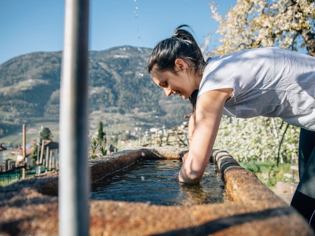 Frau hält ihre Hände in das kalte erfrischende Wasser eines Trogs